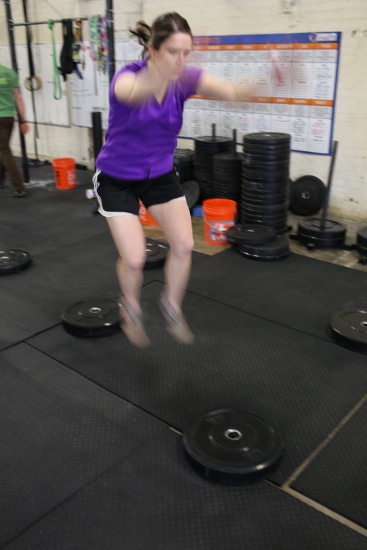 Woman jumping from weight plate to weight plate.