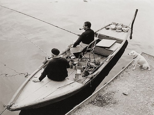 Vintage men in fishing boat smoking pipes near dock.