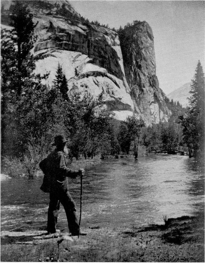 John Muir standing by river and canyon with walking stick.