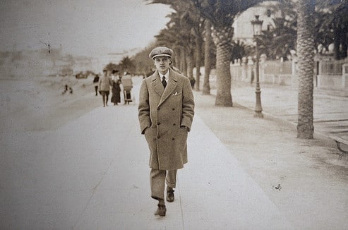 Vintage man walking down sidewalk with overcoat flat cap.